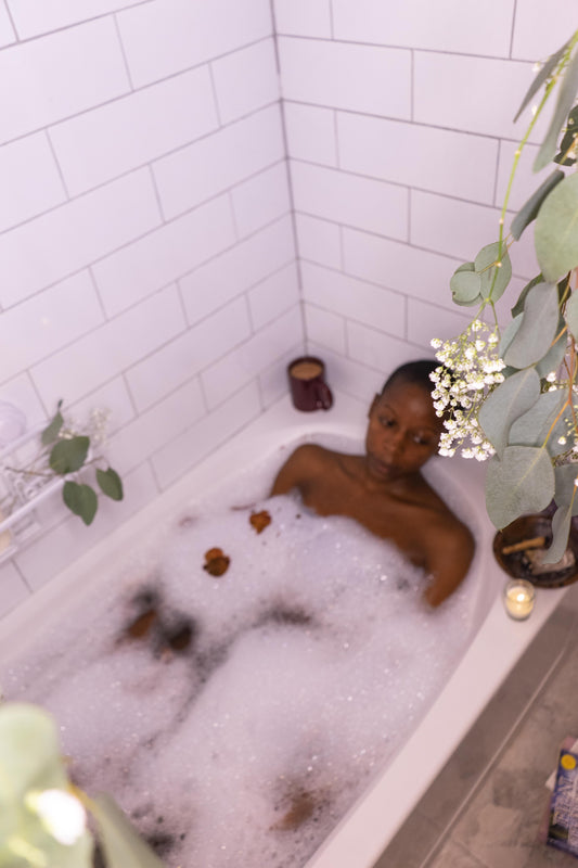 pictured is a beautiful woman taking a bubble bath with her self-love bath blend, with a cup of tea and candles lit.