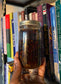 a beautiful batch of herb and spice infused sun-dried tomatoes in a glass jar, pictured in front of a collection of self-help and spiritual books